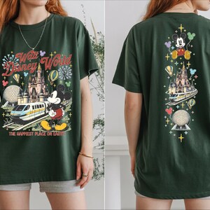 A woman wearing a green t-shirt with a Disney World-themed design, including Mickey Mouse, a castle, and a train.