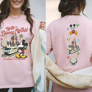 A woman wearing a pink t-shirt with a Disney World theme and various Disney characters and landmarks printed on it.