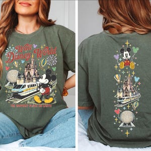 A woman wearing a green t-shirt with a Disney World-themed design, including Mickey Mouse, a castle, and various Disney-related elements.