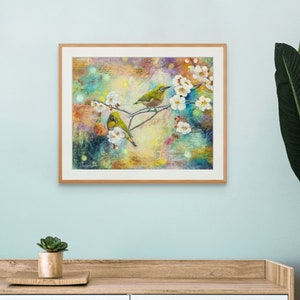 May include: A framed painting of two green birds perched on a branch with white blossoms. The background is a colorful abstract design with hints of blue, green, yellow, and orange.