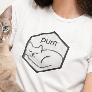 May include: White t-shirt with a black graphic of a sleeping cat and the word "purrr". A light grey cat with blue eyes is being held. A teal square with a white cat silhouette is in the upper left corner.