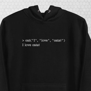 May include: Black hoodie with a front pocket and a drawstring hood. The text "cat("I", "love", "cats!") I love cats!" is printed in white. The hoodie also features "the coding {cats}" logo. The word "Black" is printed in the upper right corner.