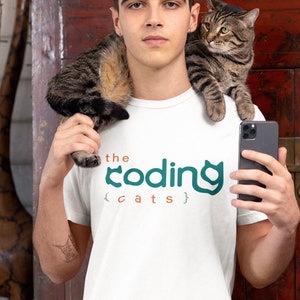 May include: White t-shirt with the text "the coding cats" in teal and orange. A tabby cat sits on the person's shoulder. The person holds a smartphone. A teal cat logo is in the upper left corner.