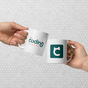 May include: Two white ceramic mugs with the text "the coding (cats)" and a teal cat logo. One mug has the full logo, the other has the logo and the text. The mugs are held up in a celebratory gesture.