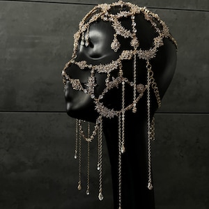 May include: A gold-toned face mask with crystal embellishments and dangling chains. The mask is designed to cover the forehead, eyes, nose, and mouth.