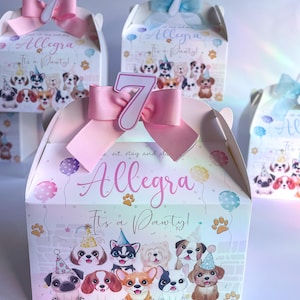 May include: A white favour box with a pink bow and a white number 7 on top. The box has a colourful design with cartoon dogs and the text "Allegra It's a Pawty!"