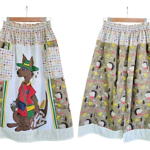 May include: A long skirt with a whimsical design. The front features a kangaroo wearing a hat and carrying luggage. The skirt has a white base with patchwork and a brown and white pattern with hedgehogs. The hem is trimmed with white fabric.