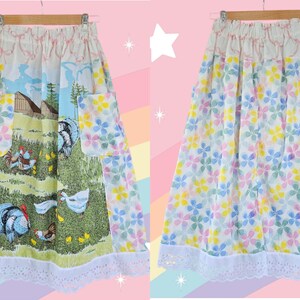 May include: A vintage skirt with a whimsical design. One side features a pastoral scene with turkeys, chickens, and a barn. The other side is covered in colorful floral patterns. The skirt has a white lace trim and pockets.