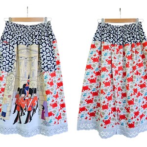May include: A-line skirt with a unique design. The top section features a navy blue floral pattern, transitioning to a cream-colored panel with a building illustration and red-coated figures. The lower half showcases a white background with red crabs. The skirt has a white eyelet lace hem.