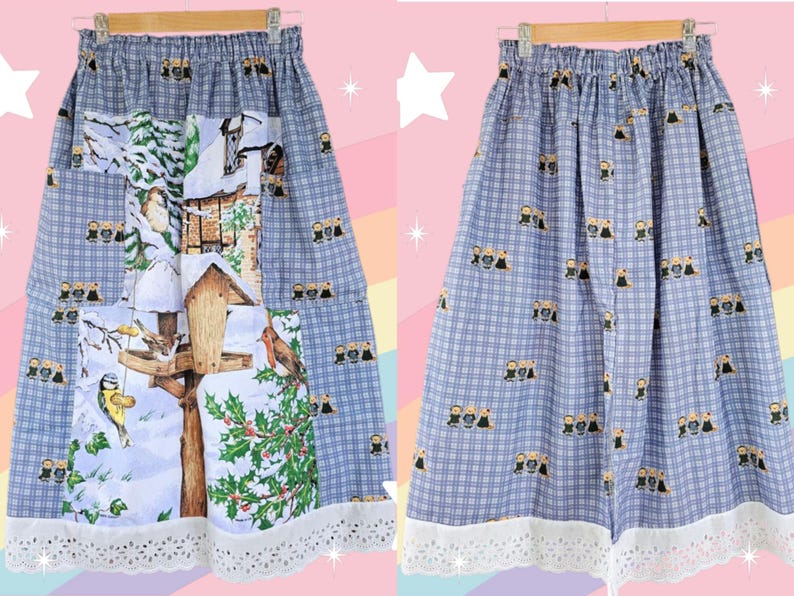 May include: A-line skirt with a blue and white plaid pattern. The skirt features a winter scene with birds, a birdhouse, and holly. The hemline is trimmed with white lace. The skirt is hanging on a wooden hanger.