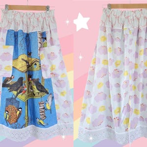 May include: A white skirt with a birdhouse and bird print on a blue background, and a cloud pattern on the sides. The skirt has pockets and a lace trim. The skirt is hanging on a wooden hanger.