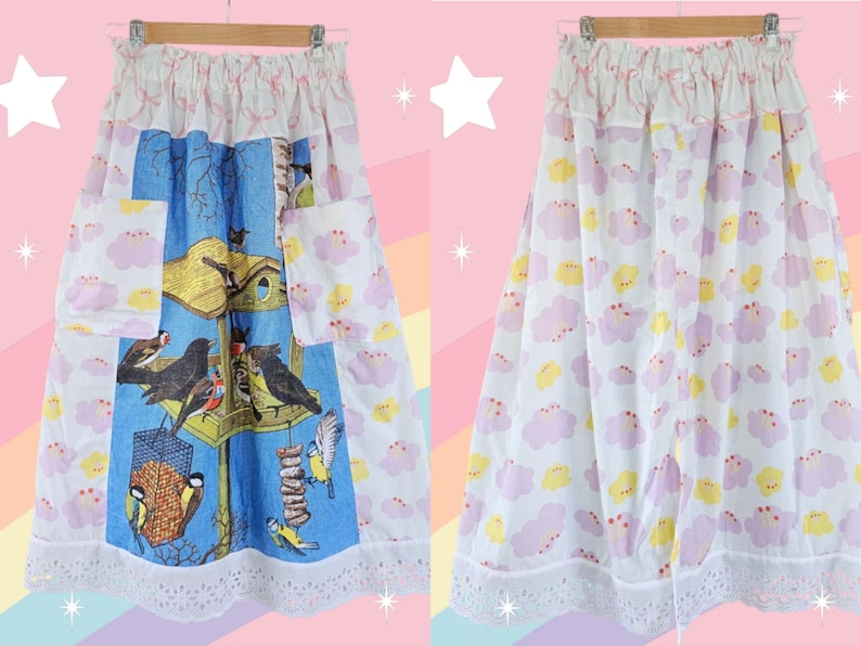 May include: A white skirt with a birdhouse and bird print on a blue background, and a cloud pattern on the sides. The skirt has pockets and a lace trim. The skirt is hanging on a wooden hanger.