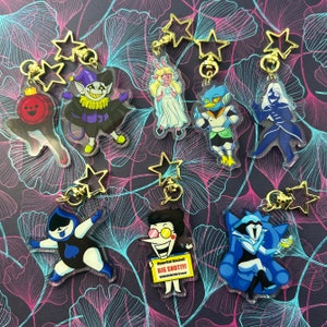 Könnte beinhalten: Ein Set mit zehn bunten Charakter-Schlüsselanhängern, die verschiedene Charaktere aus dem Videospiel Deltarune zeigen. Die Schlüsselanhänger sind aus klarem Acryl gefertigt und haben einen goldenen Metallring zum Anbringen an einer Tasche oder einem Rucksack. Die Charaktere sind Kris, Susie, Ralsei, Lancer, King, Rouxls Kaard, Jevil, Noelle, Berdly und Spamton NEO.