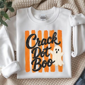 May include: A white crewneck sweatshirt featuring a graphic print of vertical orange brushstrokes. Overlaid is the black text "Crack Dot Boo" in a cursive script font, accompanied by a small, off-white cartoon ghost with a surprised expression.