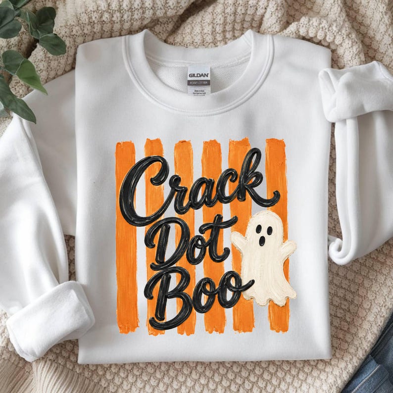 May include: A white crewneck sweatshirt featuring a graphic print of vertical orange brushstrokes. Overlaid is the black text "Crack Dot Boo" in a cursive script font, accompanied by a small, off-white cartoon ghost with a surprised expression.