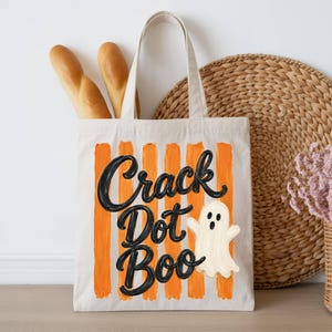 May include: A cream-colored canvas tote bag featuring vertical orange stripes and the black text Crack Dot Boo. A small white ghost illustration is positioned to the right of the text. The bag has two top handles and a rectangular shape.