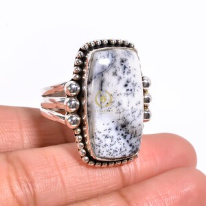 May include: A silver ring with a white and black dendritic agate stone. The stone is set in a rectangular bezel with a beaded border. The ring band is silver and has a textured design.