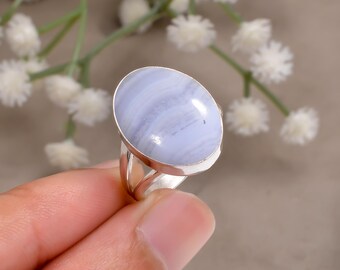 Könnte beinhalten: Ein Silberring mit einem großen, ovalen blauen Spitzenachat-Edelstein. Der Stein zeigt ein weiches, gebändertes Muster in Hellblau und Weiß. Der Ring hat ein schlichtes, poliertes Silberband-Design.