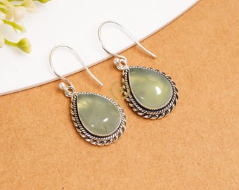 May include: A pair of silver dangle earrings with green teardrop-shaped stones. The stones are set in a silver bezel with a twisted wire design.
