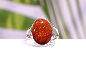 May include: A silver ring with a large oval-shaped red sunstone gemstone. The ring has a simple design with a smooth band and a bezel setting for the stone.
