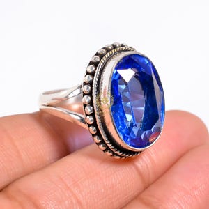 Könnte beinhalten: Ein silberner Ring mit einem großen, ovalen blauen Edelstein, der in einer Zargenfassung sitzt. Der Ring hat eine Perlenband.
