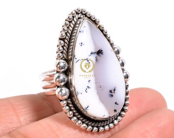 Puede incluir: Un anillo de plata con una piedra preciosa de ópalo dendrítico blanco y negro. El anillo tiene un diseño de cuentas alrededor de la piedra.
