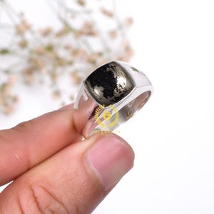 Puede incluir: Un anillo de sello de plata con una piedra cuadrada negra y dorada.