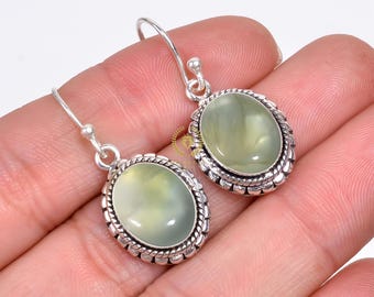 May include: A pair of silver earrings with green gemstone oval drops. The earrings have a detailed silver border around the stones.