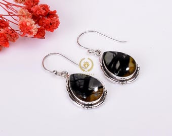 May include: A pair of silver dangle earrings with black and yellow teardrop-shaped stones. The stones have a unique pattern and are set in a silver bezel.
