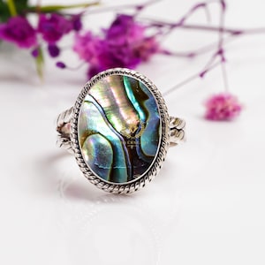 May include: A silver ring with a large oval abalone shell inlay. The shell has iridescent green, blue, and purple colors.