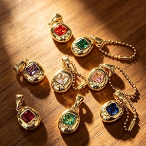 May include: A selection of gold-coloured pendants, each with a different coloured gemstone. The gemstones are square or rectangular, in colours such as red, green, purple, white, pink, and blue. Some pendants have small, clear accent stones.