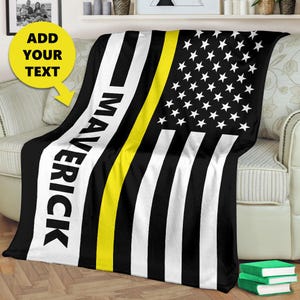 May include: Black and white American flag blanket with a yellow stripe across the middle. The text "Maverick" is printed on the left side of the blanket.