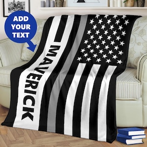 May include: Black and white fleece blanket with a thin silver stripe and the American flag design. The blanket has the word "Maverick" printed on the left side.