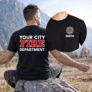 May include: Black t-shirt with white and red text that reads "YOUR CITY FIRE DEPARTMENT" on the back. The front of the shirt has a firefighter emblem and the name "SMITH" in white. The shirt is short-sleeved.