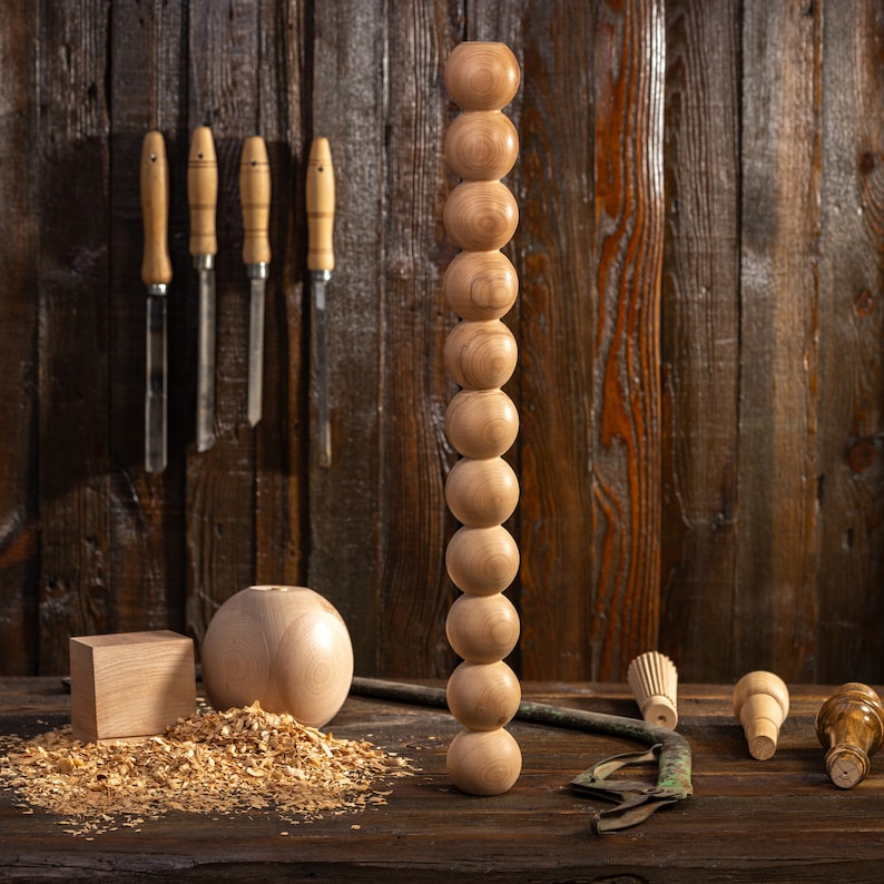 May include: A wooden dowel with a series of round wooden beads stacked on top of each other. The dowel is standing upright on a wooden surface. There are wood shavings around the base of the dowel.