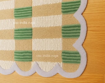 May include: Close-up of a beige, green, and white patterned rug with a scalloped edge. The rug features a checkerboard design with alternating stripes and green rectangular accents. The rug is on a wooden floor.