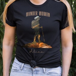 Puede incluir: Camiseta negra con un gr&aacute;fico de una excursionista con una mochila y bastones de senderismo. El texto "Wander Woman" est&aacute; por encima del gr&aacute;fico y el nombre "Alina" est&aacute; por debajo del gr&aacute;fico.