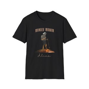 Puede incluir: Camiseta negra con un gr&aacute;fico marr&oacute;n de un excursionista con una mochila y el texto "Wander Woman" sobre el gr&aacute;fico y "Alina" debajo del gr&aacute;fico.