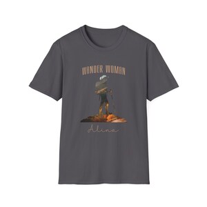 Puede incluir: Una camiseta gris oscuro con la silueta de un excursionista con una mochila y bastones de senderismo. El texto "Wander Woman" est&aacute; por encima del excursionista y el nombre "Alina" est&aacute; por debajo del excursionista.