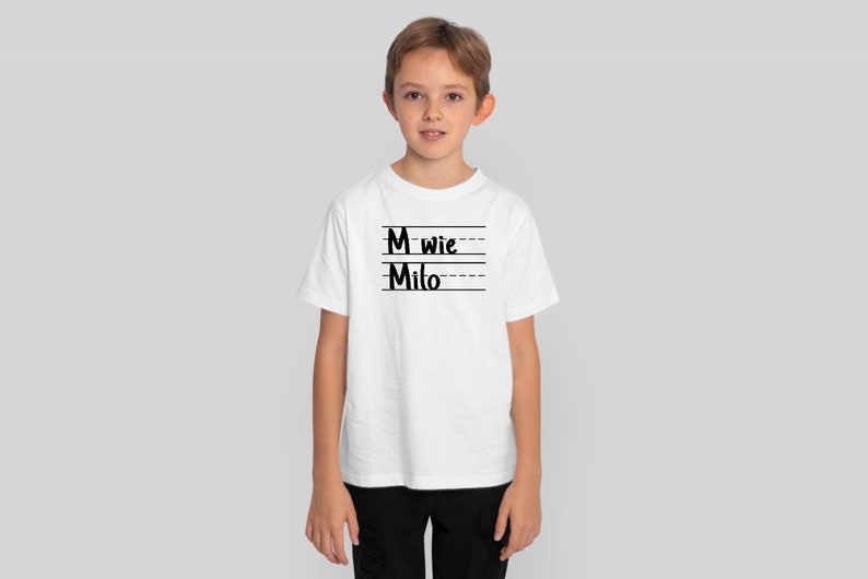 May include: White t-shirt with black text that says "M wie Milo" on it. The text is written in a handwritten style.