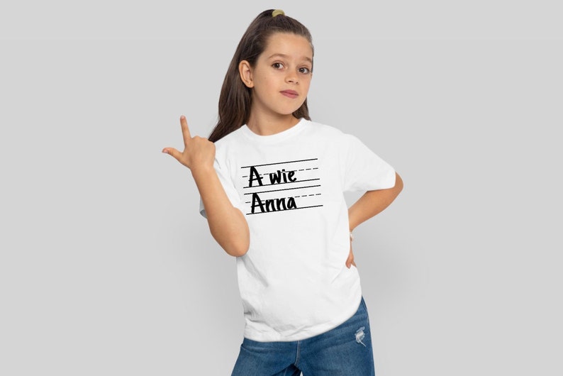 May include: White t-shirt with black text that says "A wie Anna" on it. The text is written in a handwritten style.