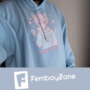 May include: Light blue hoodie with a graphic of an anime-style character with cat ears, holding a small cat. The hoodie has the words "Cutie Pie" and "Femboy Mage" printed on it, along with hearts, stars, and bubble tea illustrations.