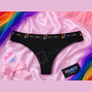 Könnte beinhalten: Schwarzer Tanga mit einem breiten elastischen Bund, der den Schriftzug FemboyZone und ein regenbogenfarbenes F-Logo aufweist. Das Kleidungsstück wird zusammen mit einer kleinen schwarzen Karte präsentiert, die den Text FEMBOY PRIDE trägt.