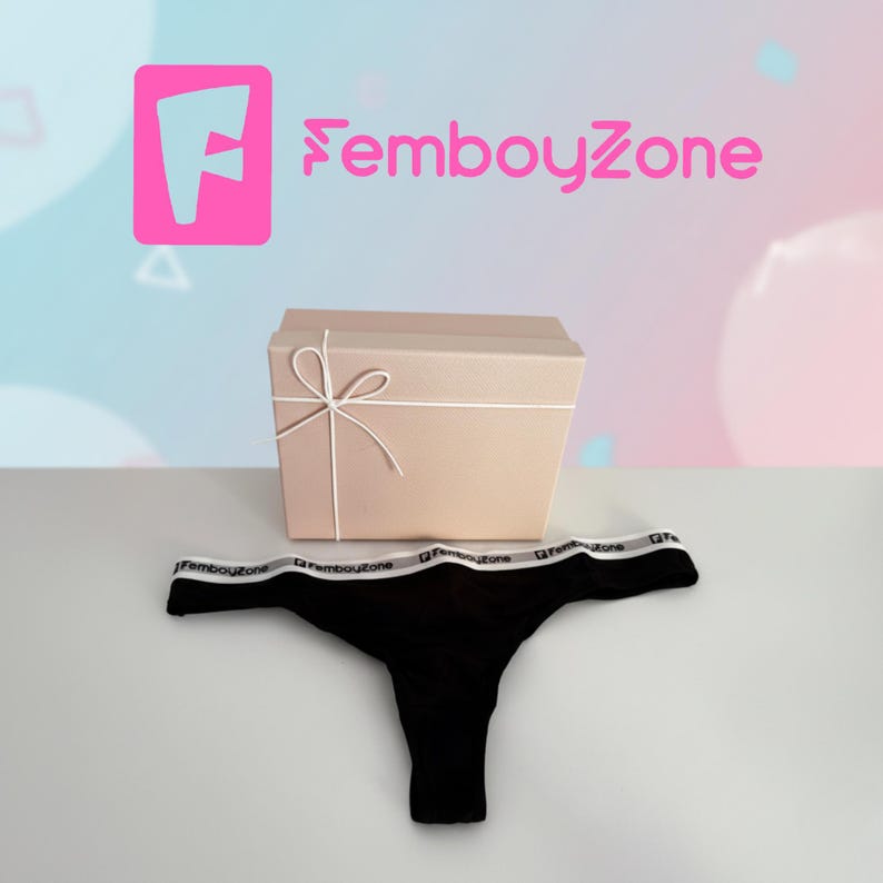 May include: Black thong underwear with a white waistband featuring the text "FemboyZone". A beige gift box tied with white string is behind the underwear. The logo "FemboyZone" is in pink.