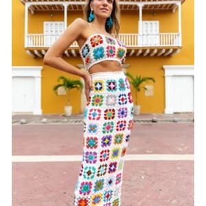 Puede incluir: Un conjunto de top y falda de crochet blanco con un patrón geométrico colorido. El top es sin tirantes y la falda es de largo midi.