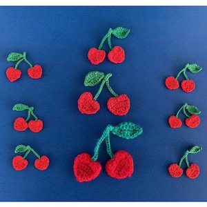May include: A collection of ten crocheted cherries in various sizes. The cherries are red with green stems and leaves. The cherries are arranged on a blue background.