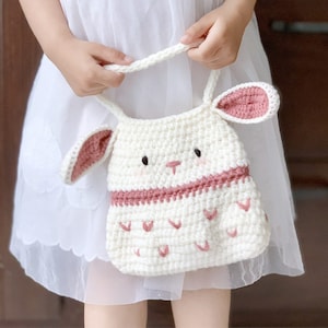 May include: A white crocheted bunny-shaped bag with pink ears and a pink trim. The bag has a white crocheted strap.