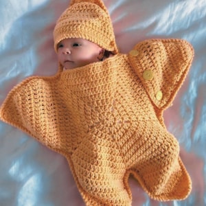 Peut inclure: Un sac de couchage pour bébé en crochet en forme d'étoile de mer, avec un bonnet en crochet assorti. Le sac de couchage est de couleur orange clair.