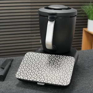 以下が含まれることがあります： シルバーのハンドルと模様入りの蓋が付いた、黒とシルバーの電気ケトル。 ケトルは、お揃いの模様入りのプレートが付いた黒いベースの上にあります。 黒いアクセサリーが左側にあります。