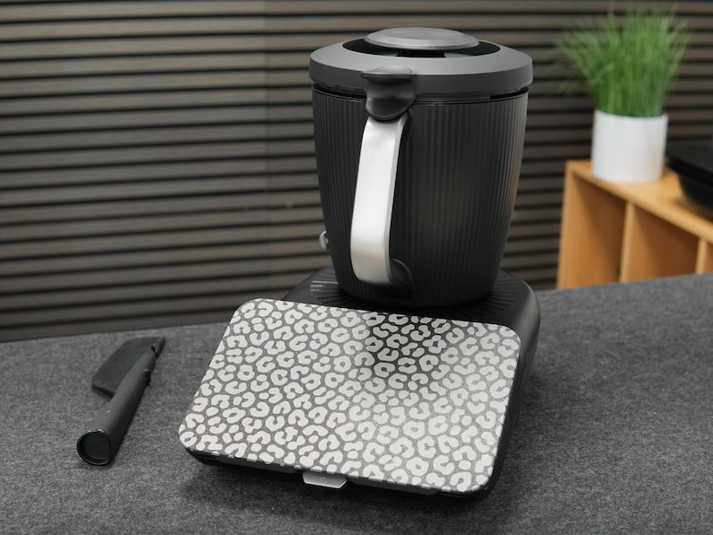 以下が含まれることがあります： シルバーのハンドルと模様入りの蓋が付いた、黒とシルバーの電気ケトル。 ケトルは、お揃いの模様入りのプレートが付いた黒いベースの上にあります。 黒いアクセサリーが左側にあります。